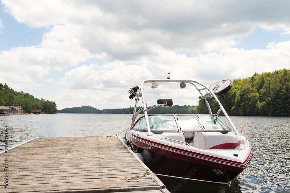 A wakeboard boat at a wooden dock in the Muskokas on a sunny day.