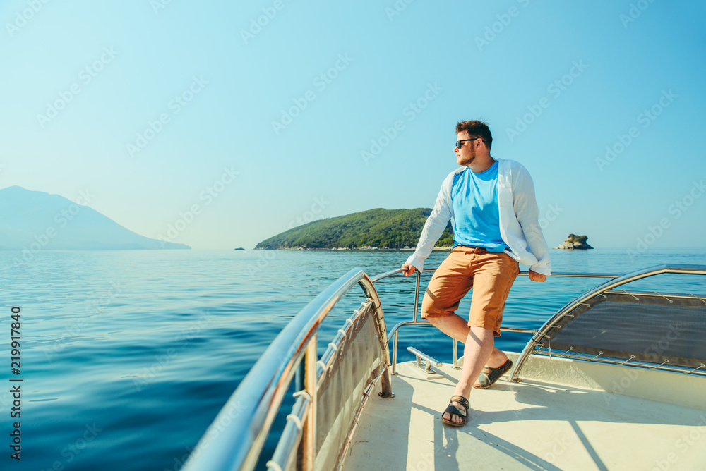 success man standing at nose of boat with sea and mountains on background