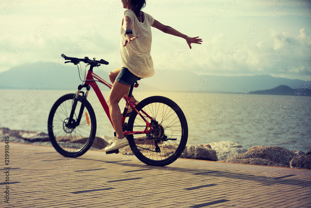 Fototapeta premium handsfree woman riding a bike on sunny seaside with arms outstretched