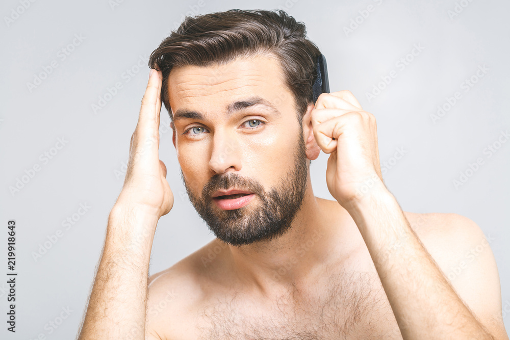 Portrait of handsome young man combing his hair in bathroom. Isolated over grey background. Portrait of handsome young man combing his hair in bathroom. Isolated over grey background.