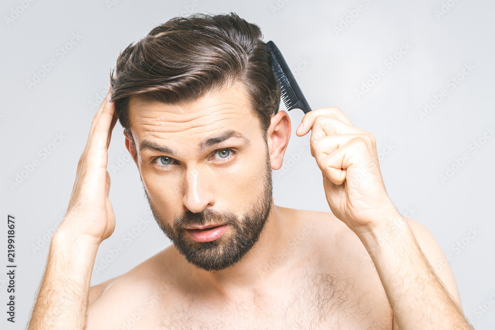 Portrait of handsome young man combing his hair in bathroom. Isolated over grey background. Portrait of handsome young man combing his hair in bathroom. Isolated over grey background.