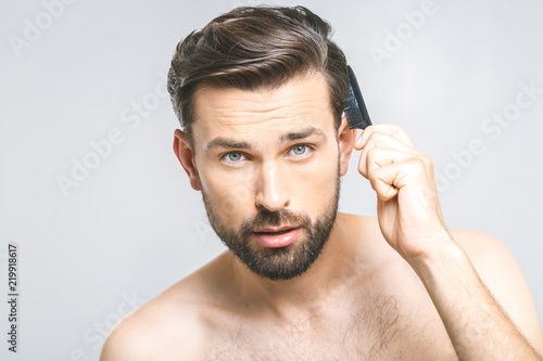 Portrait of handsome young man combing his hair in bathroom. Isolated over grey background.