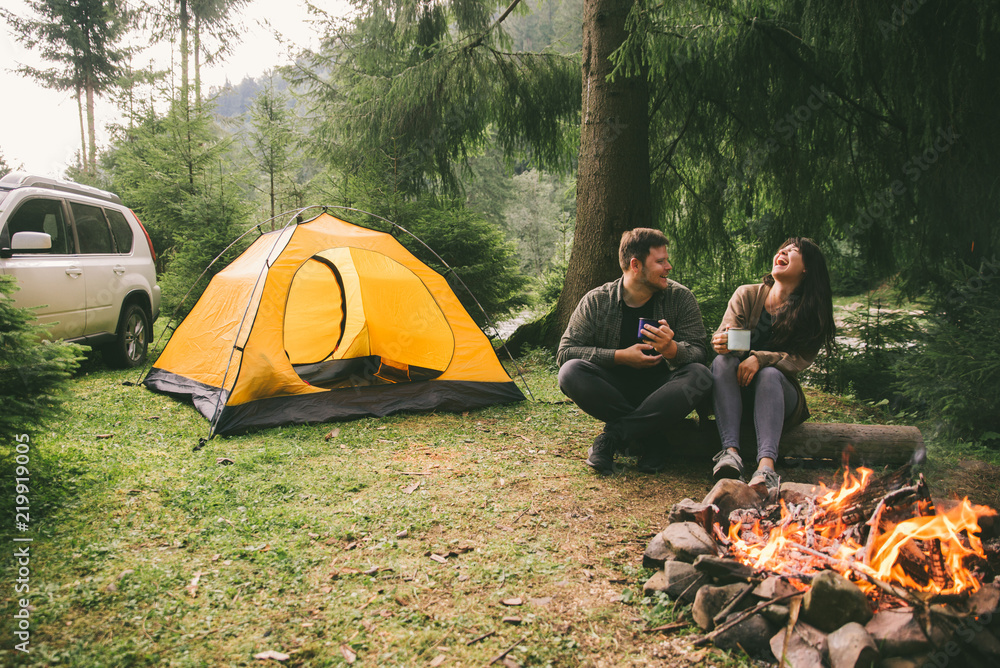 couple sitting near fire and drink hot tea. hiking concept. - obrazy, fototapety, plakaty 