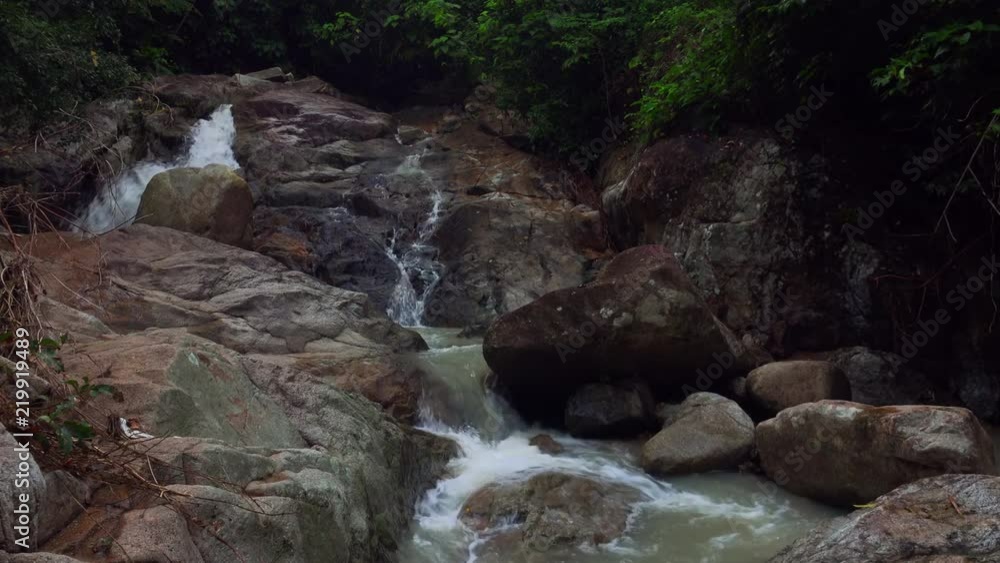 Beautiful view of river rapids. Peaceful scenery with water flowing over rocks covered with moss. Stream running over mossy boulders against trees on background. Amazing nature of Koh Samui, Thailand. Beautiful view of river rapids. Peaceful scenery with water flowing over rocks covered with moss. Stream running over mossy boulders against trees on background. Amazing nature of Koh Samui, Thailand.