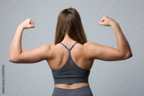 Rückenansicht einer jungen Frau im Sportdress die die Armmuskeln anspannt