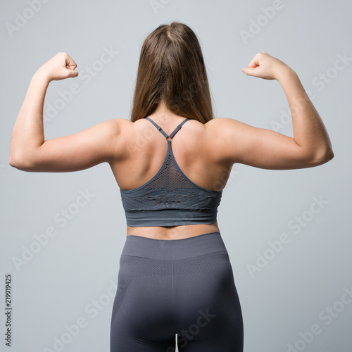 Rückenansicht einer jungen Frau im Sportdress die die Muskeln anspannt