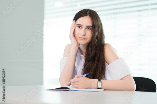 a girl in a white shirt and with her hair down sits at a table