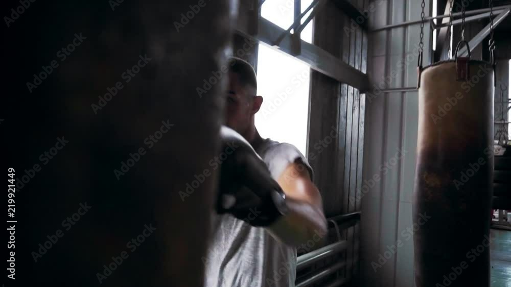 Muscular athlete working out with punching bag in gym, male boxer training. Front view Muscular athlete working out with punching bag in gym, male boxer training. Front view