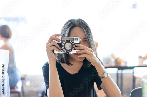 A hipster teenager is taking a film camera in the cafe.