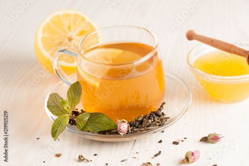 Closeup of cup of tea with tea leaves, mint on vintage wooden background. Black herbal tea with lemon, ginger and honey. hot winter drink