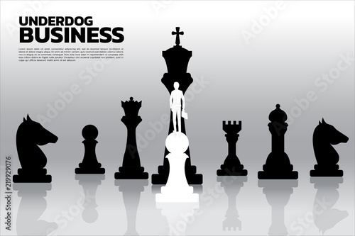 Silhouette of businessman standing on white pawn chess piece in front of all of black chess piece . Concept of underdog business marketing strategy.