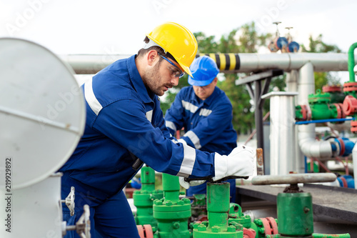 Two petrochemical workers inspecting pressure valves on a fuel tank