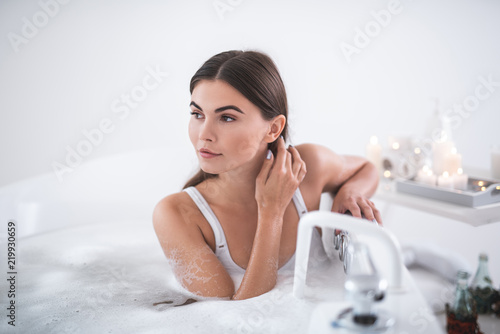 Portrait of orderly woman touching hair with hand while resting in cozy bath in apartment