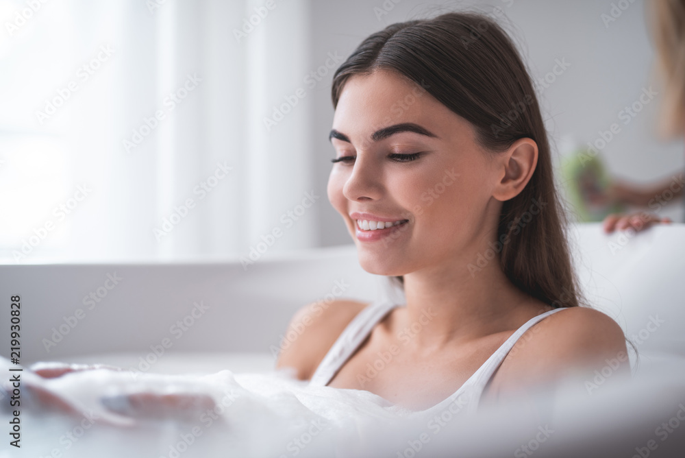 Portrait of beaming girl taking bath while entertaining. She looking at her hands in foam Portrait of beaming girl taking bath while entertaining. She looking at her hands in foam