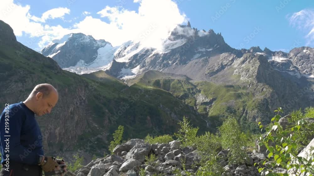 The man is facing the mountain peaks and looks into the smartphone. He chooses the route. The man is facing the mountain peaks and looks into the smartphone. He chooses the route.