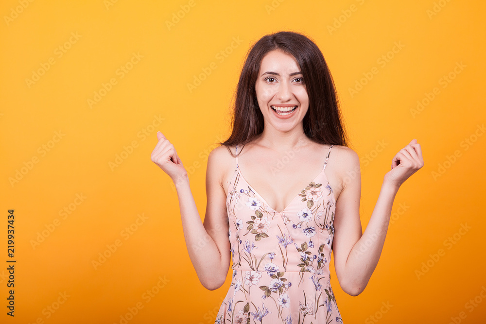 Attractive young woman smilling at the camera in studio over yellow background in short dress. Attractive young woman smilling at the camera in studio over yellow background in short dress.
