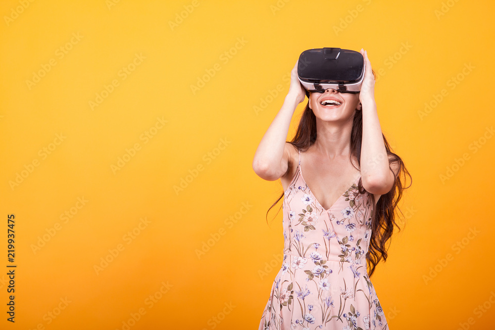 Smile happy woman getting experience using VR-headset glasses of virtual reality in studio over yellow background. Smile happy woman getting experience using VR-headset glasses of virtual reality in studio over yellow background.