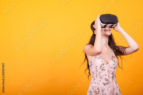 Girl plays vr game in virtual reality helmet in studio over yellow background. Studio portrait of girl playing mobile app on VR Glasses.