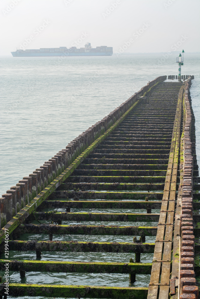 Fototapeta premium Sea near Vlissingen, Zeeland, Netherlands, old wooden pier at high tide and big cargo ship on horizon