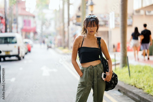 A young Asian woman commutes through the city on a bright sunny day. She is wearing trendy street clothes with her backpack. photo