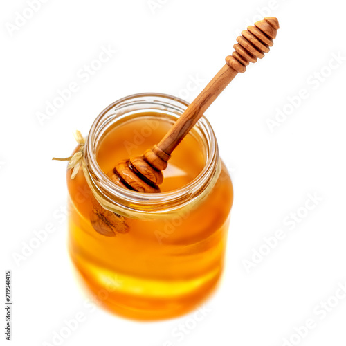 Wooden dipper with dripping honey and glass jar isolated on white background, macro