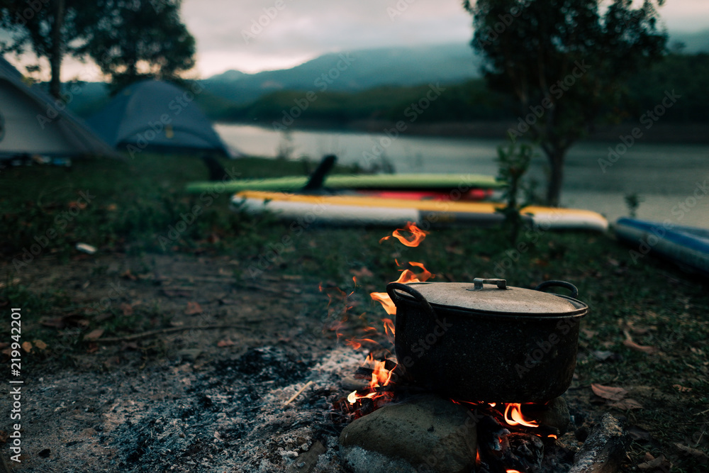 Camp and cooking in field conditions, boiling pot at the campfire on picnic in morning. Cooking dinner on firewood stove using firewood when going to the wilderness or outdoor activity, camping tent Camp and cooking in field conditions, boiling pot at the campfire on picnic in morning. Cooking dinner on firewood stove using firewood when going to the wilderness or outdoor activity, camping tent