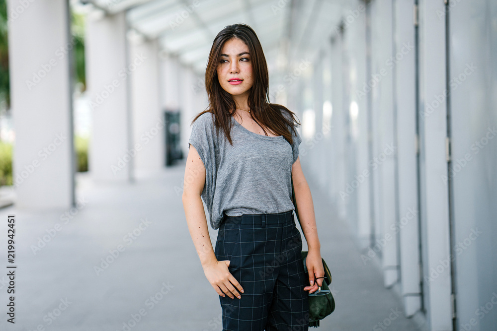 A portrait of a young attractive Japanese woman strolling through the city. She is wearing a comfortable top and jeans.