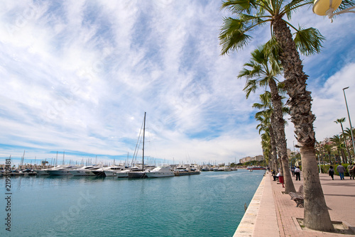 Fototapeta Naklejka Na Ścianę i Meble -  Beautiful port of Alicante, Spain at Mediterranean sea. Luxury yachts, ships, ferries and fishing boats sailing and standing in rows in harbor. Rich people traveling around the world. Sunny evening