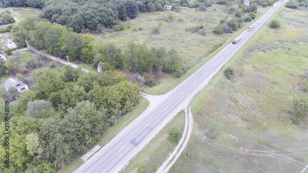 Aerial view of white car driving on country road in forest. The aerial view flew over an old patched two-lane forest road with moving green trees of dense forests growing on both sides. Driving a car