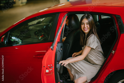 Canvas Print A portrait of a young smiling Japanese woman getting inside a red car which she booked using a ride hailing app on her smartphone