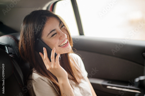 A young Japanese lady is talking on her smartphone while seated at the backseat of a ride hailing car. She looks like she is having a fun-filled conversation. © Danon