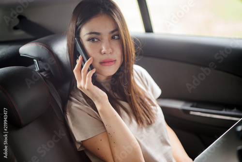 A young Japanese lady is talking on her smartphone while seated at the backseat of a ride hailing car. She looks like she is having a serious conversation. © Danon