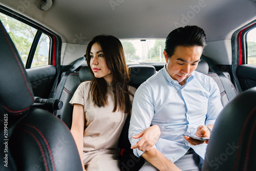 A young attractive Japanese woman leans toward her boyfriend as they ride a car which they booked from a ride hailing app. She is tired yet happy from their trip. © Danon