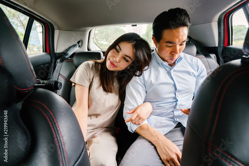 A young attractive Japanese woman leans toward her boyfriend as they ride a car which they booked from a ride hailing app. She is tired yet happy from their trip.