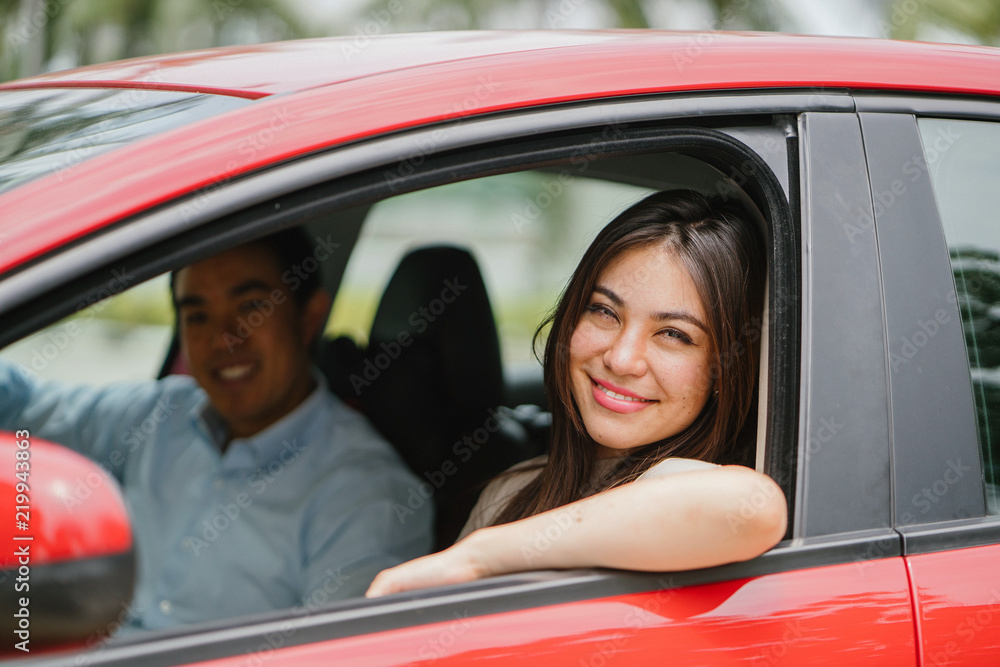 Portrait of a young Japanese Asian woman leaning out the window of a red car window and smiling happily. She is being driven to her destination in a ride she booked on a ride hailing app. Portrait of a young Japanese Asian woman leaning out the window of a red car window and smiling happily. She is being driven to her destination in a ride she booked on a ride hailing app.