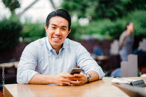 Canvas Print A portrait of a young Japanese man using his smartphone while seated outdoors on a bright day