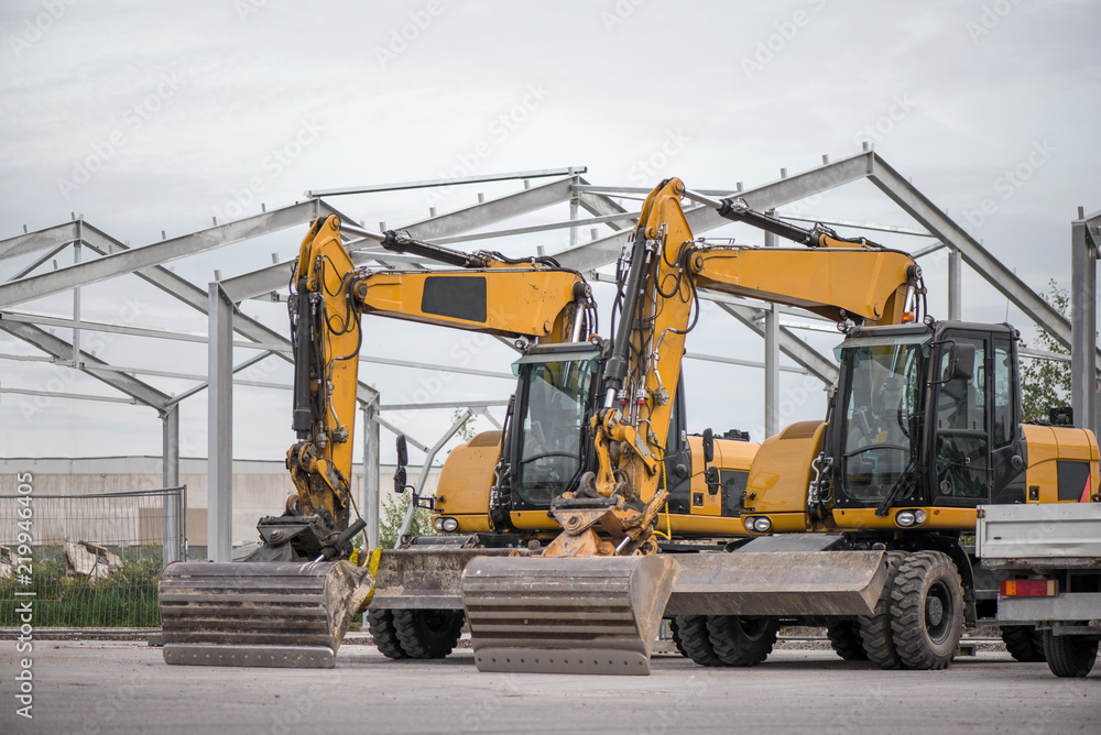 Multiple cars, excavators, trucks, loaders, concrete mixers and construction machinery in large parking lot in industrial territory, next to concrete and asphalt factory