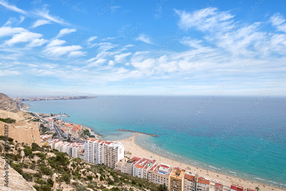 Fototapeta premium Panoramic view of Postiguet beach from Santa Barbara Castle in Alicante, Spain. Sunny day at Mediterranean sea. Block apartment buildings in a row. Palm trees and vibrant blue water.