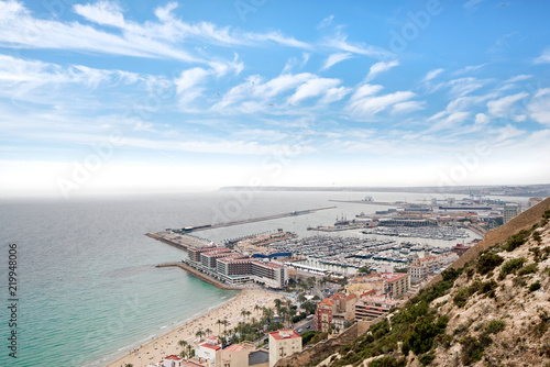 Panoramic view of Postiguet beach  from Santa Barbara Castle in Alicante, Spain. Sunny day at Mediterranean sea. Block apartment buildings in a row. Palm trees and vibrant blue water. © lainen