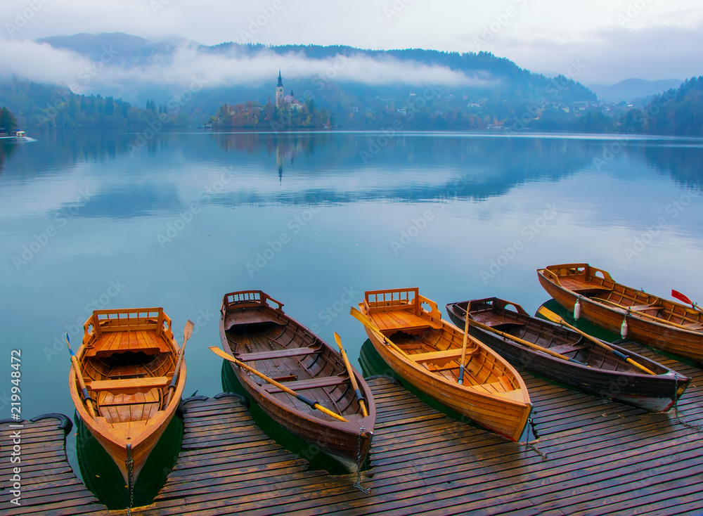Autumn scenery with boats moored on Bled lake at foggy day