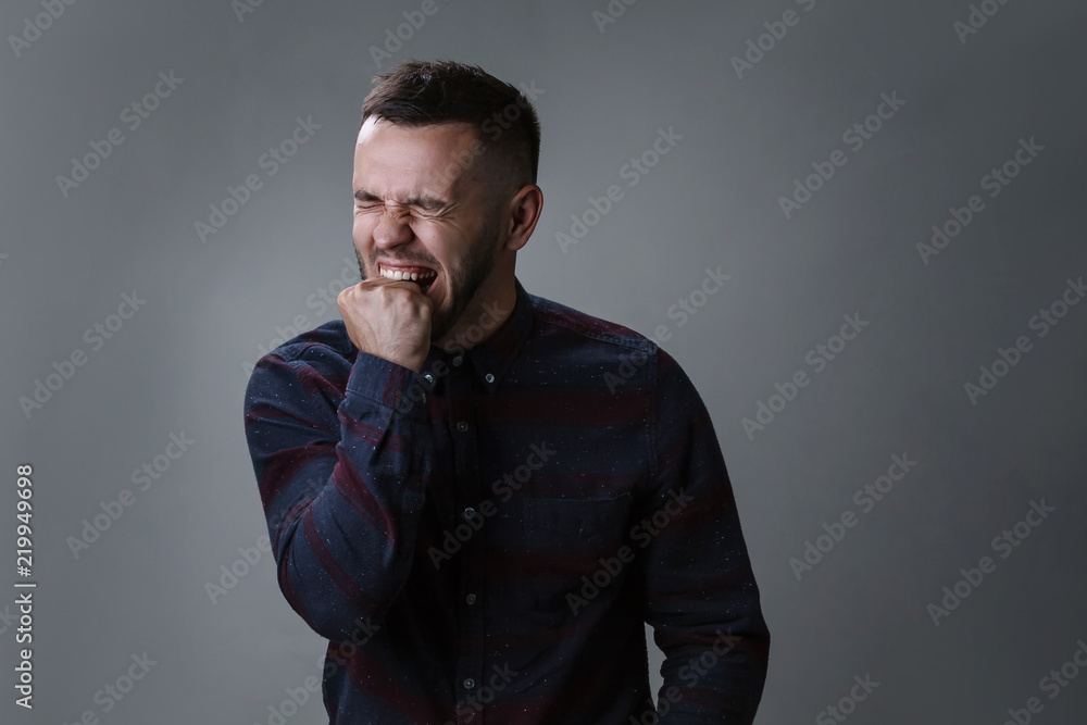 Portrait of angry and depressed man biting his fist desperate feeling frustrated and helpless in depression and sadness facial expression concept on dark gray background