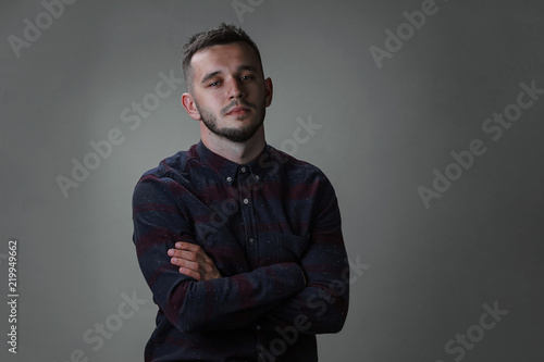 Young man studio shot portrait. Handsome in checkered shirt and cross hands on breast. Copy space dark grey background