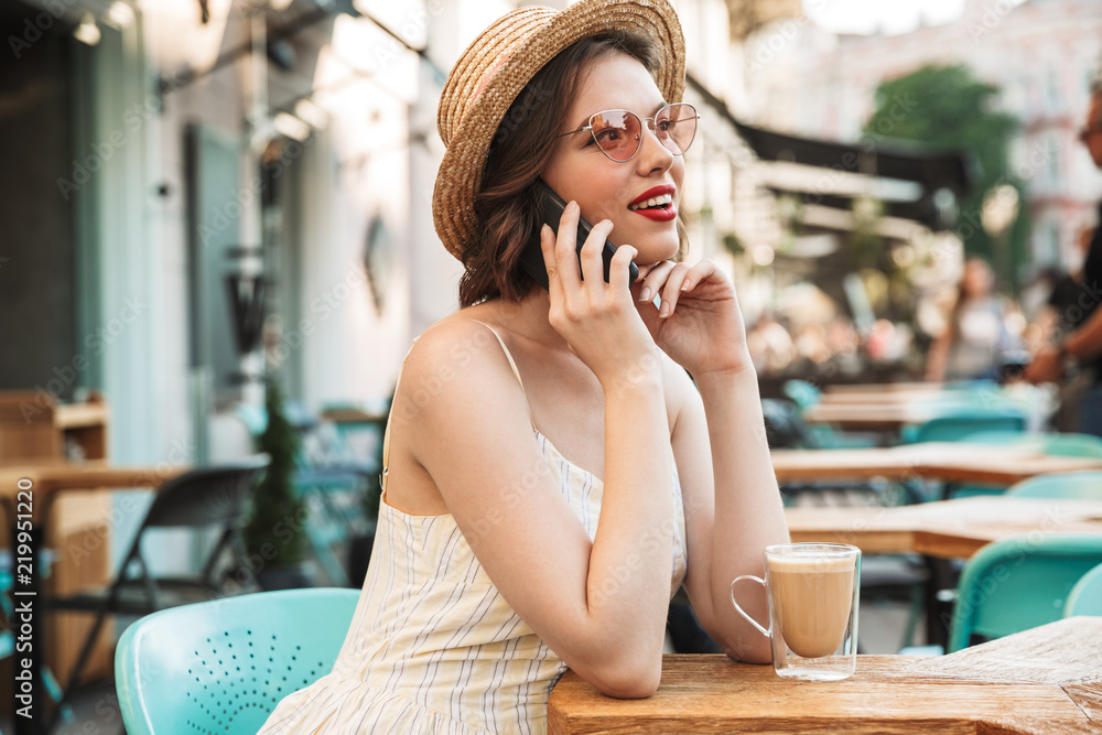 Young woman in dress and straw hat talking by smartphone