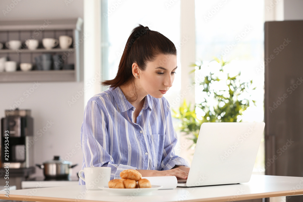 Young female freelancer working with laptop in kitchen Young female freelancer working with laptop in kitchen