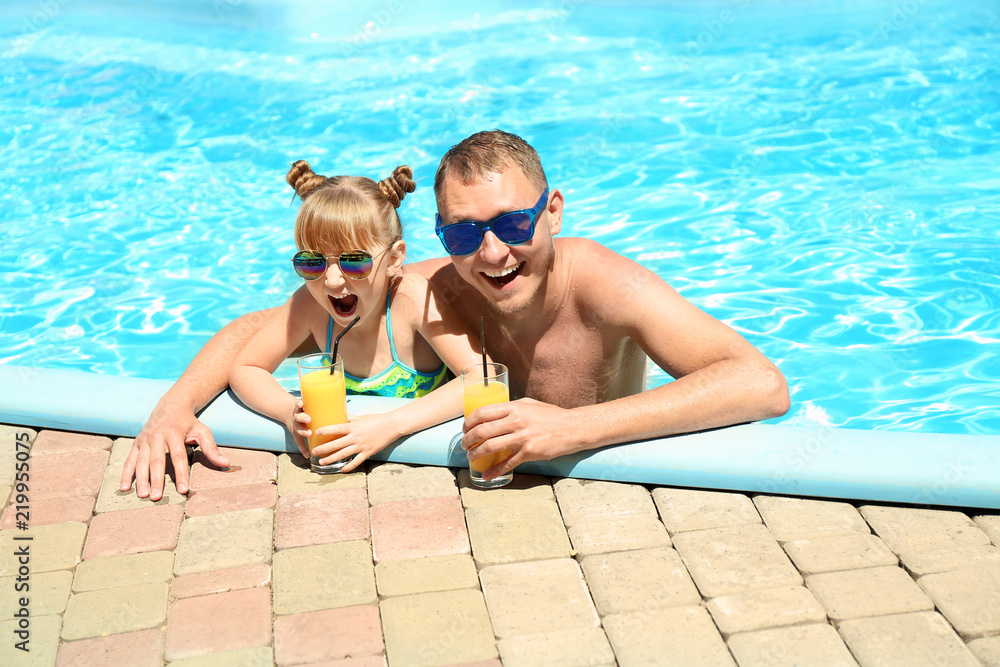 Happy father and daughter with glasses of juice resting in swimming pool