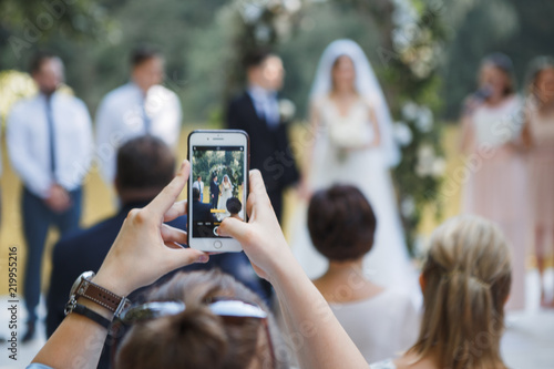Fototapeta guest at the wedding ceremony takes pictures on the phone of the newlyweds