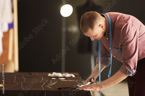 Young tailor cutting fabric...