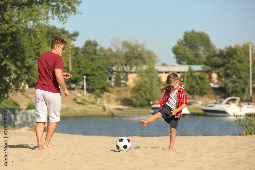 Little boy with his dad playing football on sand beach