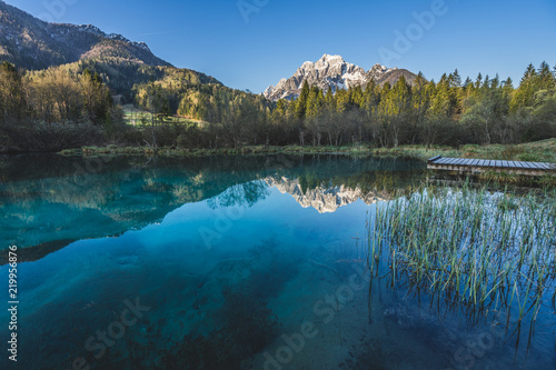 Fototapeta Naklejka Na Ścianę i Meble -  Sunrise view of Zelenci National Park and Nature reservation in Slovenia, Julian Alps. Sunset or sunrise over an alpine lake with blue water and sky. Alpine mountain landscape, river and lake.