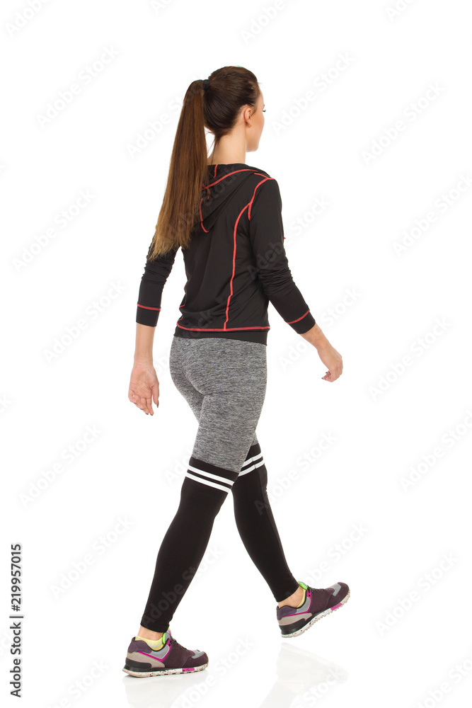 Young Woman In Sports Clothes Is Walking. Rear Side View. Young Woman In Sports Clothes Is Walking. Rear Side View.